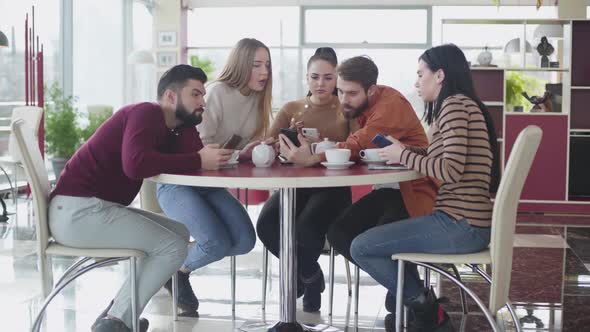 Five Caucasian Young People Looking at Smartphone Screen and Talking. Friends Using Gadgets As