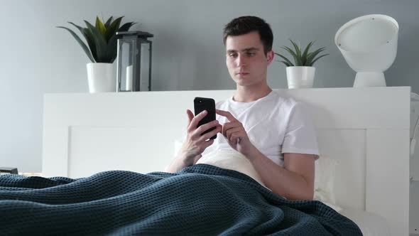 Man Using Smartphone While Lying in Bed