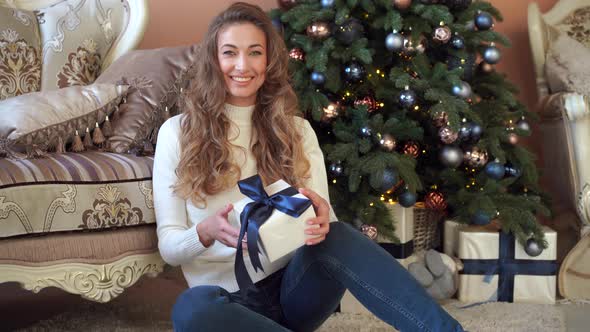 Christmas. Woman Dressed White Sweater and Jeans Sitting on the Floor Near Christmas Tree with