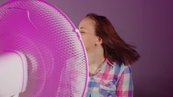 Close Up of Young Woman Waves Her Head Sitting on Chair in Front of Fan on Purple Background