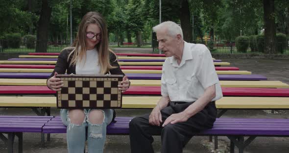 Young Girl Spends Time with an Old Man in the Park Shows Chess Him and Laughs