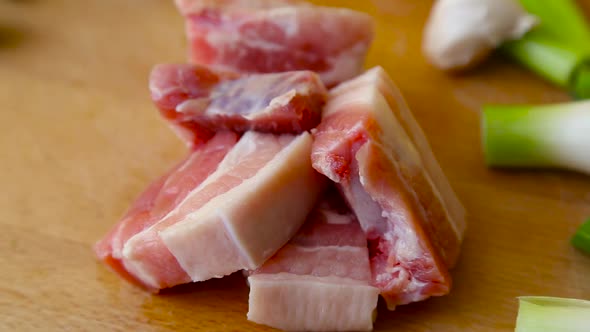 Focusing out on slices of pork belly with green onions on cutting board