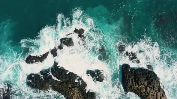 ocean blue waves break on high cliff of a rocky mountain.