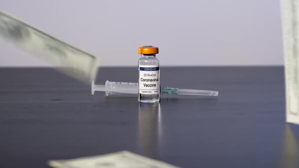 Money Falling on Table Near COVID-19 Vaccine Vial