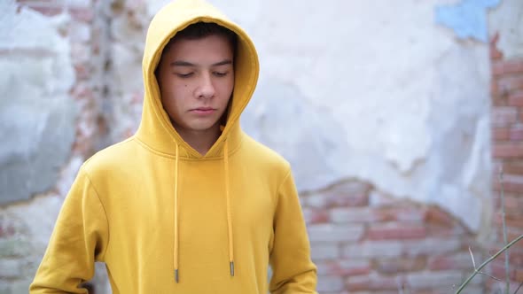 teenager in a yellow sweatshirt looks down, then raises his eyes