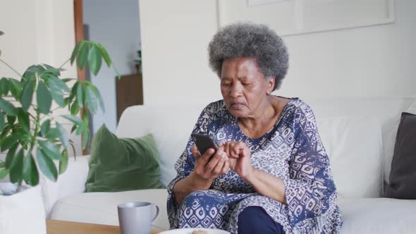 African american senior woman sitting on the couch and using smartphone