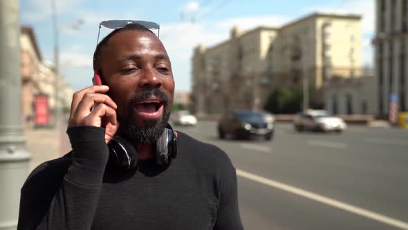 Portrait of an African Man with Glasses on Forehead and Headphones Around Neck. He Talks on the Red