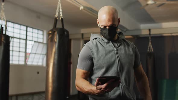 Fit caucasian man wearing face mask using digital tablet at the gym