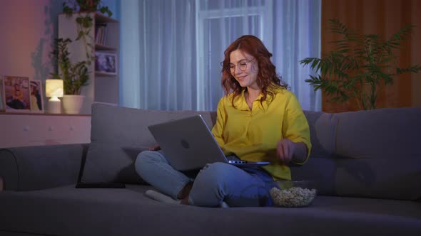 Woman Eats Popcorn and Joyfully Reacts to Good News or Won on Internet While Sitting on Couch with