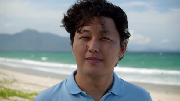 Portrait Asian Man in a Blue Shirt Standing on the Beach By the Sea Against the Backdrop of High