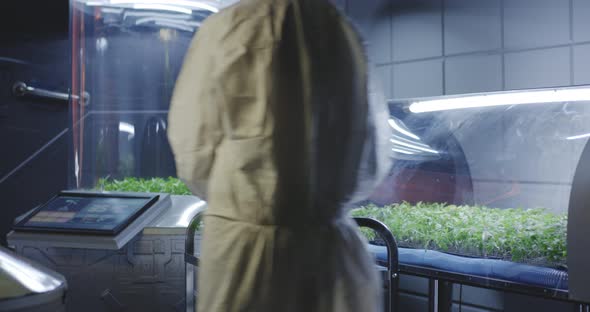 Scientist in Hazmat Suit Checking Plant Incubators alt