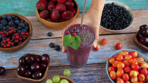 Hand Puts a Glass of Smoothies with Chia Seeds on the Wooden Table. Vegan Breakfast.