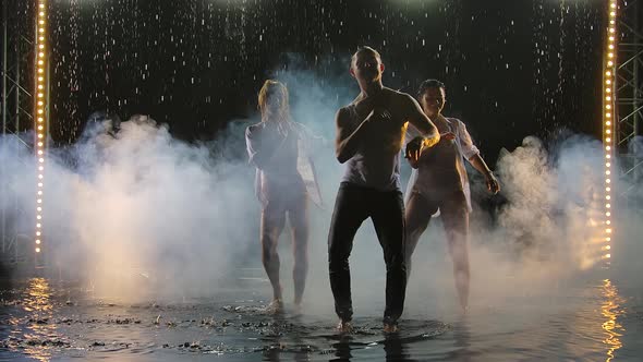 Two Women and a Man Dancing a Passionate Dance of Salsa in Raindrops on a Dark Studio Background