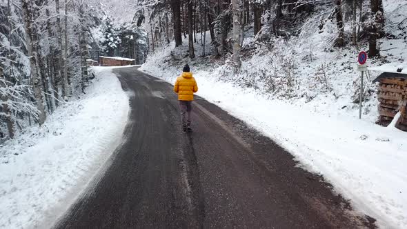 Person Walking on Forest Road in Wintry Snow Woodland, Aerial Follow