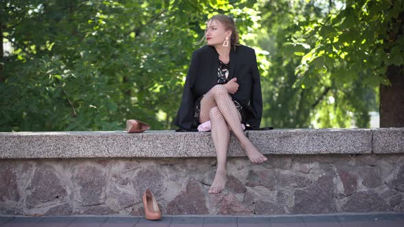 Wide Shot Tired Young Caucasian Woman Sitting in City Park with Highheels Scattered