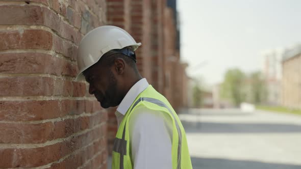 Exhausted Builder in Helmet Banging Head Against Brick Wall