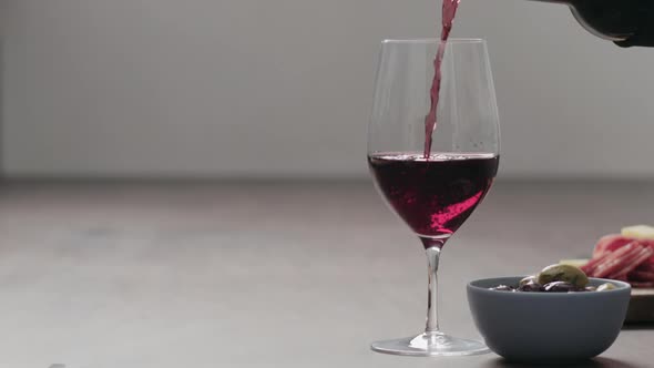 Slow Motion Pour Red Wine Into Wineglass with Appetizers on Background on Wood Table