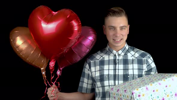 A Young Man Is Standing with a Gift and Heart-shaped Balloons, A Man Holds in His Hands a Gift and