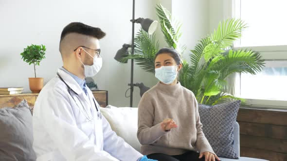 A Young Doctor Wearing Glasses and a Mask in a White Lab Coat Sits on a Sofa at a Meeting