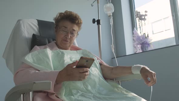 Smiling Senior Lady Having Video Call On Cellphone While Resting In The Hospital. medium shot