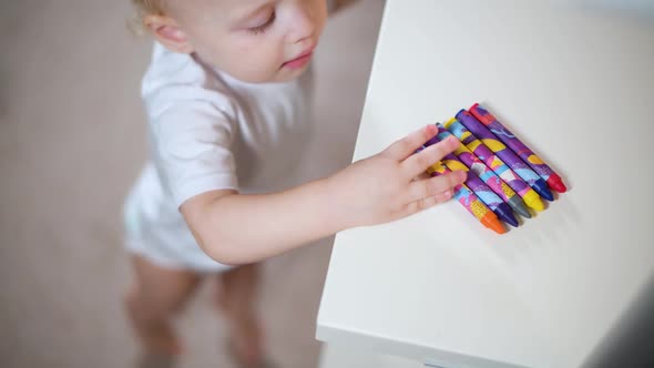 a little girl takes a crayon from a shelf and immediately begins to draw it on a white shelf