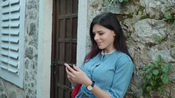 Pretty young woman with brunette hair in denim overalls  texting on her phone
