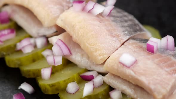 herring fillet with onion and pickled cucumber on a black plate, top view