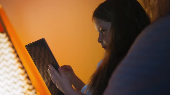 Girl Surfs Internet on Tablet Leaning on Pillows in Bed