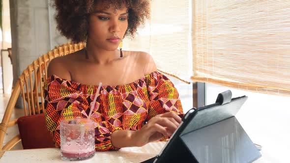 Beautiful young African woman smiling with tablet inside restaurant.