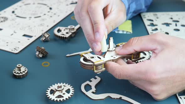 Man assembling puzzle toy at home, holding small wooden details in hands, using sandpaper