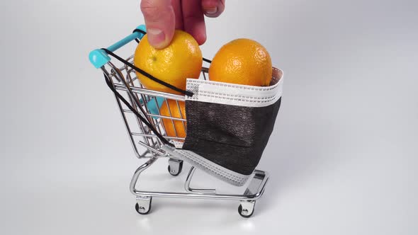 Hand takes a tangerine from a shopping cart with a medical protective mask. 