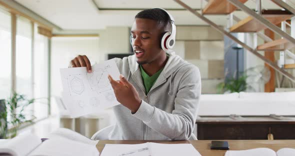 African american male teenager wearing headphones having a video conversation and using a laptop