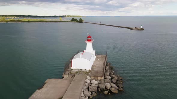 Aerial view of a white lighthouse on a lake breakwall and a boat entering the harbor on a sunny day.