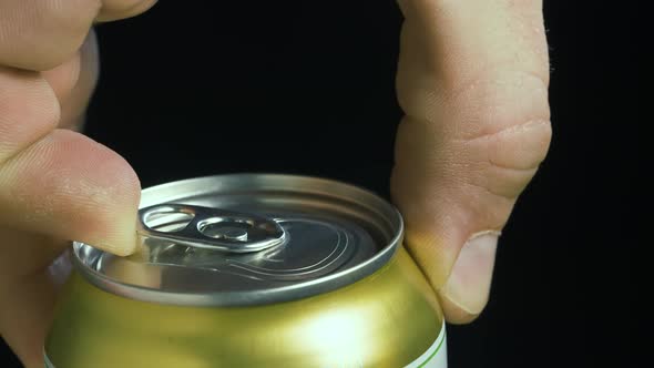 A Man's Hand Opens a Shaken Metal Can of Beer on a Black Gradient Background in Slow Motion