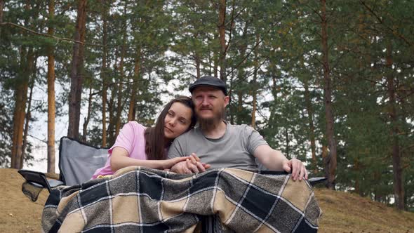 A Man and a Woman Hold Hands While Sitting in Armchairs Outdoors in a Camping Covered with a Blanket