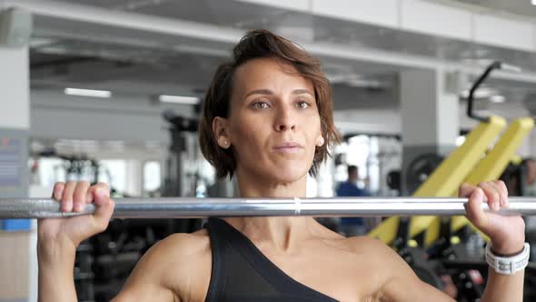 Woman is Doing Set of Reps Exercise with Barbell Lifting It Over the Head in Gym