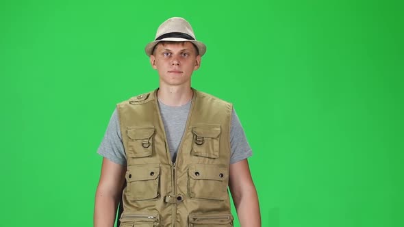 Young Man in a Grey T-shirt, Sleeveless Shirt and Hat Going Against a Green Background. Slow Motion.