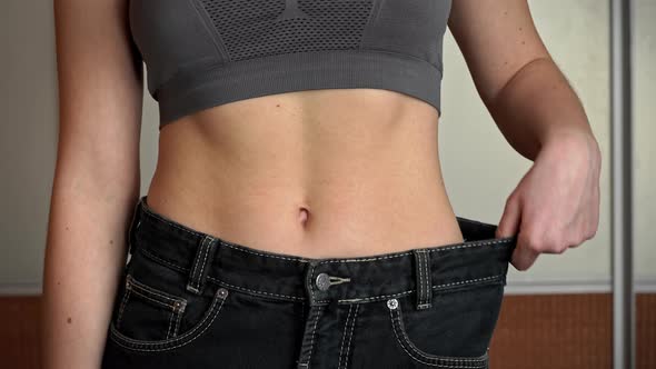 Girl with a Beautiful Figure Measures Old Big Jeans and Checks the Result