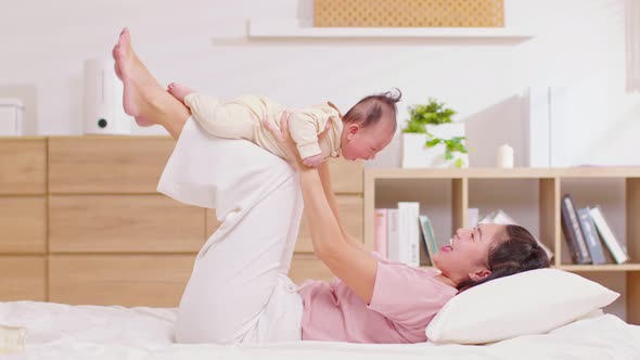 New asian mom playing to adorable newborn baby on bed smiling and happiness at home