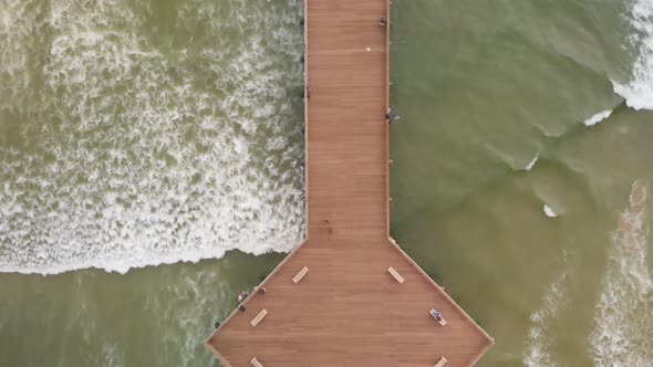 Drone Flies Over Pismo Beach Pier Looking Down at Waves and Surfers