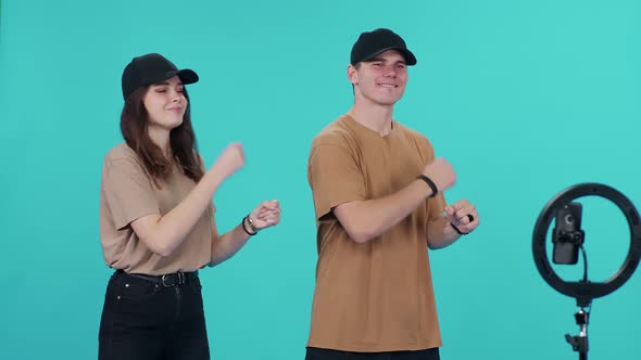 Young Couple are Synchronously Dancing to the Music on a Blue Background While Shooting a Video on