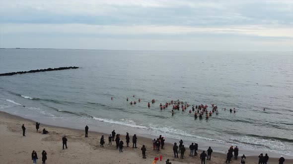 a pan right drone shot over polar bears club members in the cold Atlantic Ocean. Onlookers watch fro