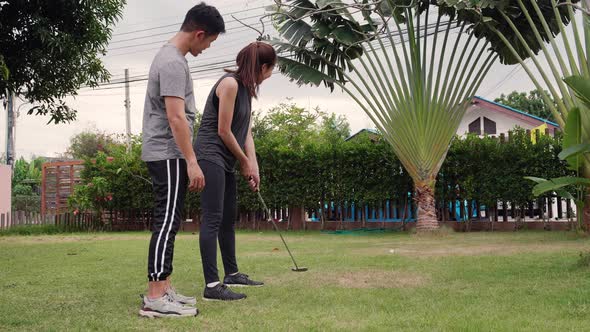 Asian young A couple training together to play golf on the behalf of the grass on vacation