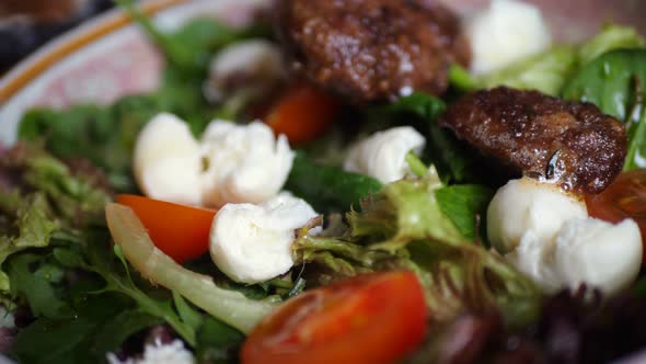 Cook Hands Placing Fresh Grilled Meat on Plate with Tomato Salad in Restaurant Kitchen