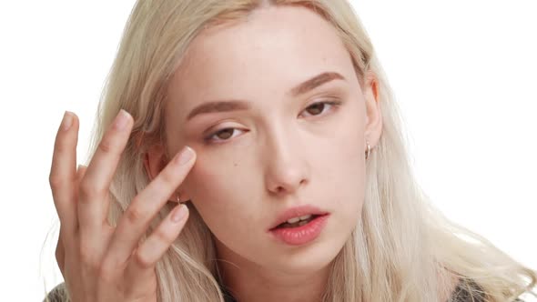 Young Attractive Caucasian Blonde Teenage Girl on White Background Combing Hair Touching Face