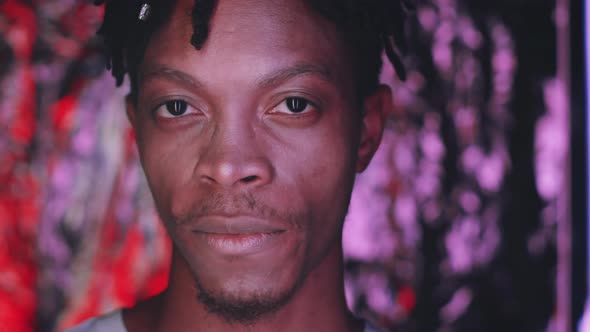 Young African Man Taking of Sunglasses and Smiling at Camera in Neon Light