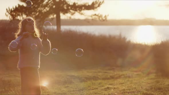 Girl Blowing Bubbles In Field At Sunset