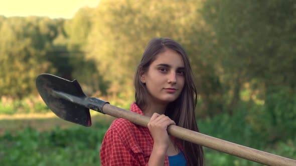 Beautiful young girl farmer with a shovel on the field.