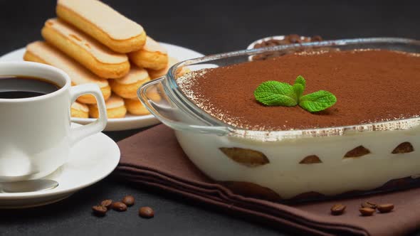 Tiramisu Dessert in Glass Baking Dish, Cup of Espresso Coffee and Savoiardi on Concrete Background