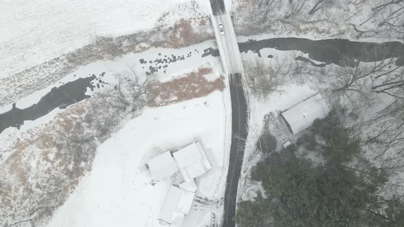 Drone view of lone car on snowy country road in Wisconsin. Bridge over creek running through farm. alt